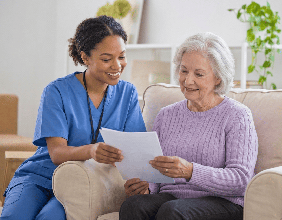A nurse sitting with an older woman on a couch, reviewing a medical bill together