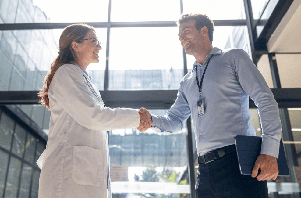 A clinician and a hospital administrator shaking hands in a bright modern hospital lobby